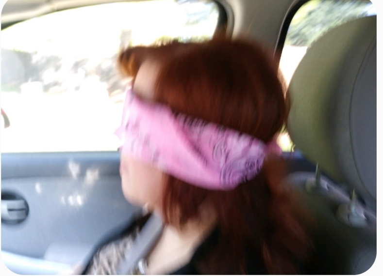 Blurry photo of Kat wearing a pink bandana blindfold in the car.
