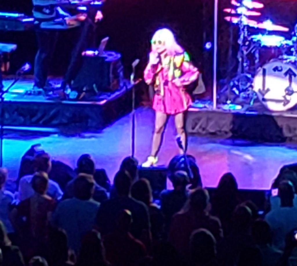 Debbie Harry onstage wearing a pink outfit with pink tips in her blonde hair.