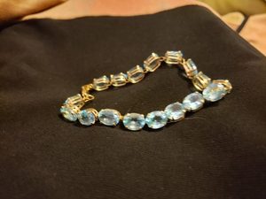 Gold tennis bracelet set with oval blue topaz stones, resting on dark fabric. Kat originally gave the bracelet to her best friend as her something blue on her wedding day.